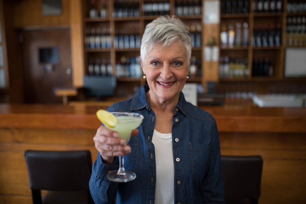 A woman at a bar holds up her cocktaill and smiles