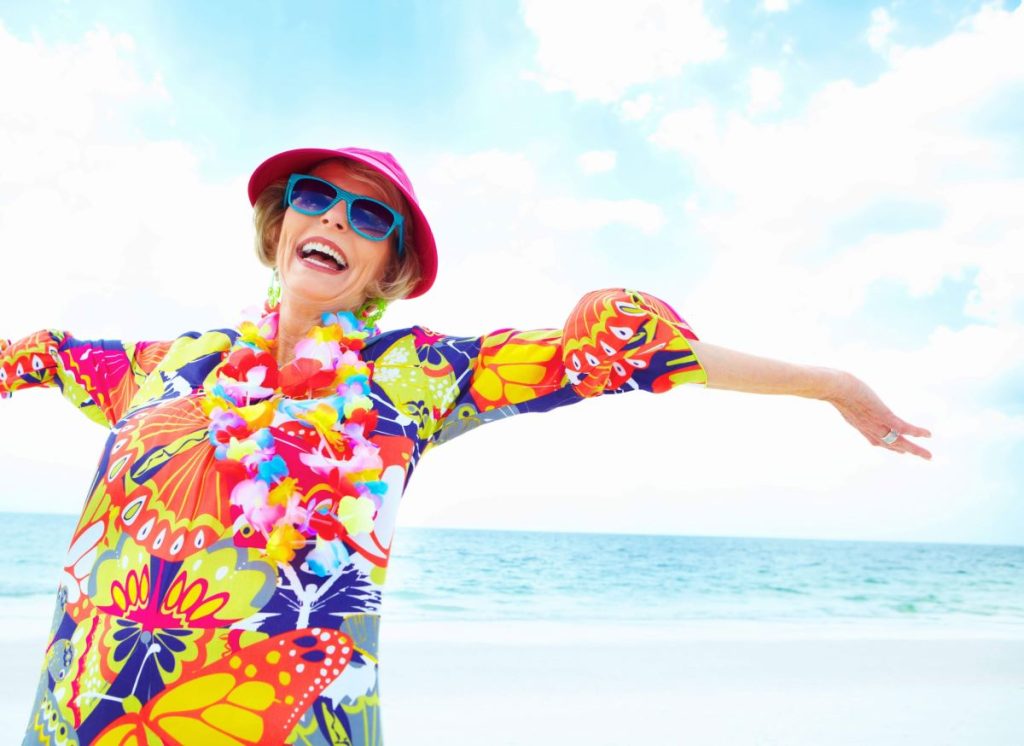 A woman ina colorful outfit smiles and dances on the beach