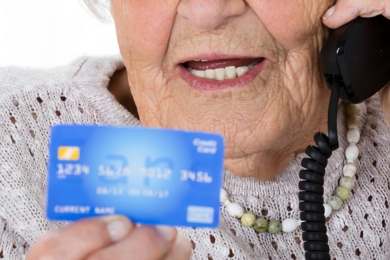 Older woman talking on the phone and holding a credit card.