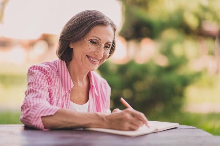 Older woman writing on a notebook.