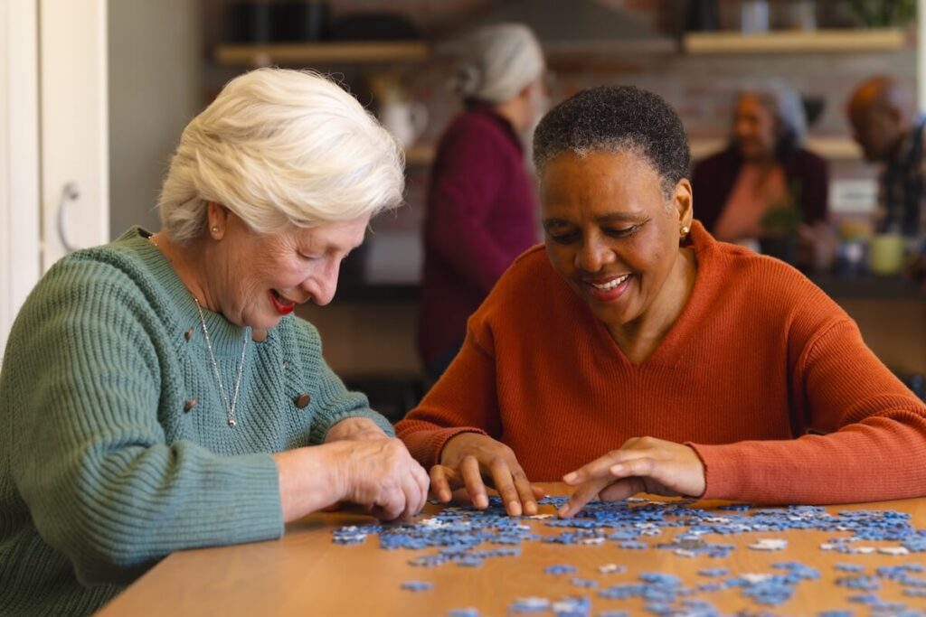 alternative therapies for dementia Happy diverse senior female friends playing with jigsaw puzzles in sunny dining room at home. Retirement, friendship, wellbeing, activities,